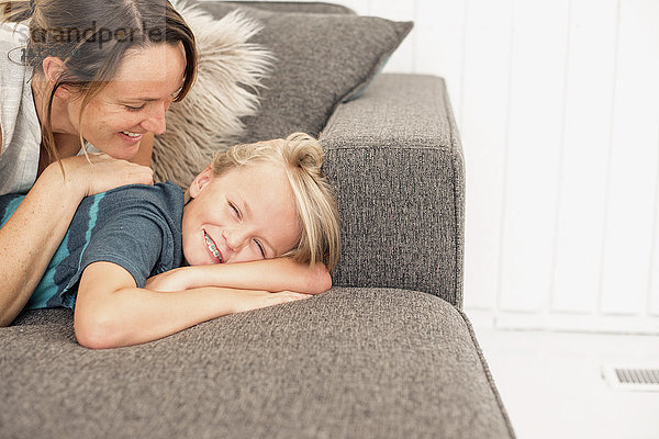 Lächelnde Mutter und Sohn liegen auf einem Sofa.