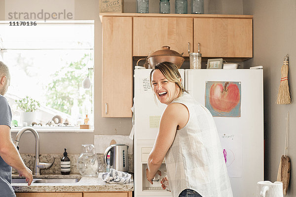 Lächelnde blonde Frau  die an einem Kühlschrank in einer Küche steht.