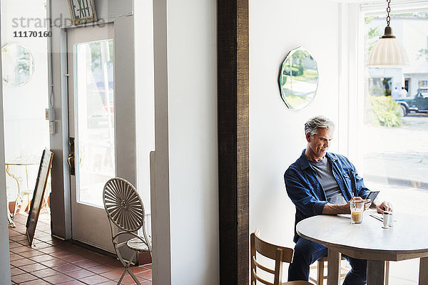 Ein Mann sitzt an einem Coffeeshop-Tisch und schaut auf sein Smartphone.