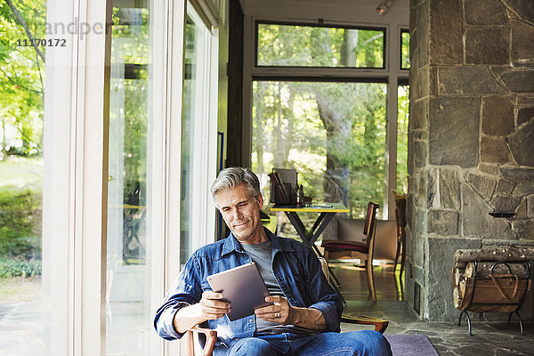 Ein am Fenster sitzender Mann liest mit einem digitalen Tablett.