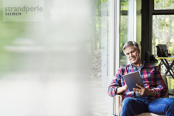 Ein am Fenster sitzender Mann liest mit einem digitalen Tablett. Unscharfer Vordergrund.