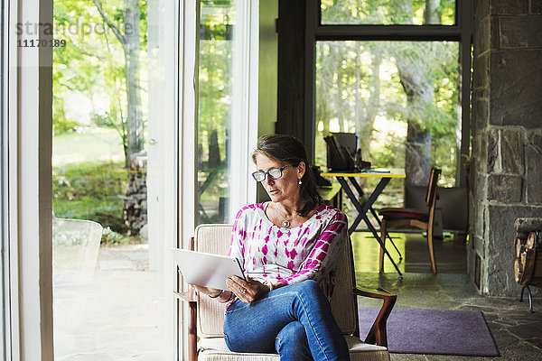 Eine Frau  die an einem Fenster sitzt und ein digitales Tablett hält.