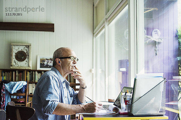 Ein Mann  der zu Hause an einem Schreibtisch sitzt und an einem Laptop-Computer arbeitet.