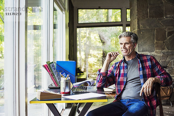 Ein Mann  der zu Hause an einem Schreibtisch mit einem Laptop-Computer sitzt und Kopfhörer trägt.