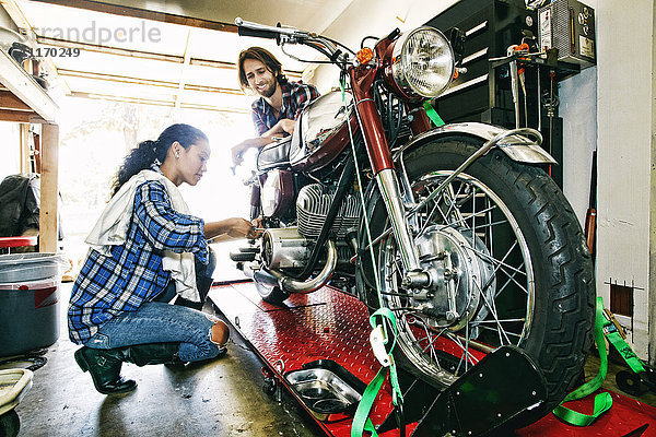 Mann beobachtet Frau bei der Reparatur eines Motorrads in der Garage