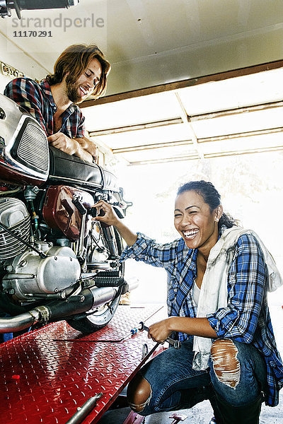 Mann beobachtet lachende Frau bei der Reparatur eines Motorrads in der Garage