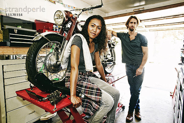 Seriöser Mann und Frau posieren mit Motorrad in Garage