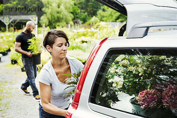 Auto in einem Gartencenter geparkt  eine Frau lädt Blumen in den Kofferraum.
