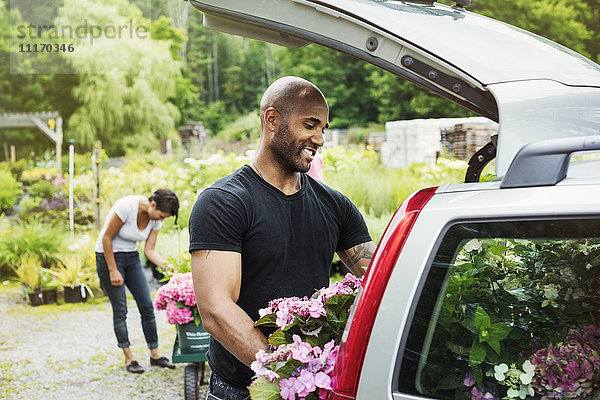 Auto in einem Gartencenter geparkt  ein Mann lädt Blumen in den Kofferraum.