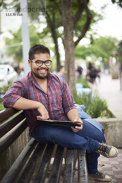 Lächelnder hispanischer Mann sitzt auf einer Bank und liest eine Broschüre