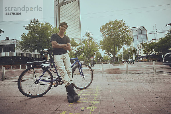 Lächelnder hispanischer Mann  der sich in der Stadt auf ein Fahrrad stützt