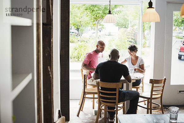 Zwei Männer und eine Frau sitzen an einem Tisch in einem Cafe und essen zu Mittag.