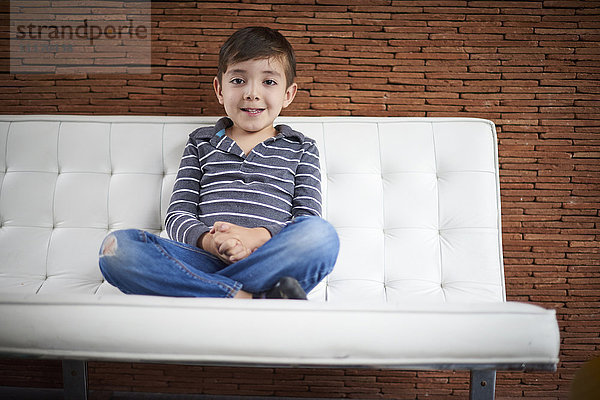 Hispanischer Junge sitzt im Schneidersitz auf dem Sofa