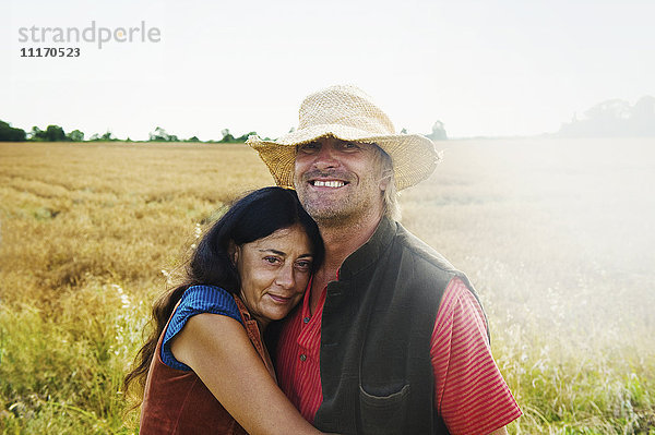 Ein Mann und eine Frau halten im Sommer auf einem Feld Händchen.