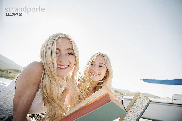 Zwei blonde Schwestern liegen auf einem Steg und lesen ein Buch.