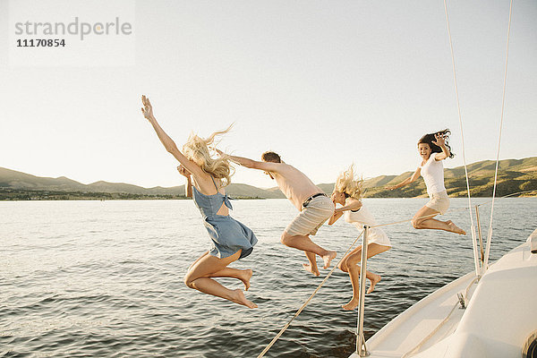 Vier Personen springen von der Seite eines Segelbootes in einen See.