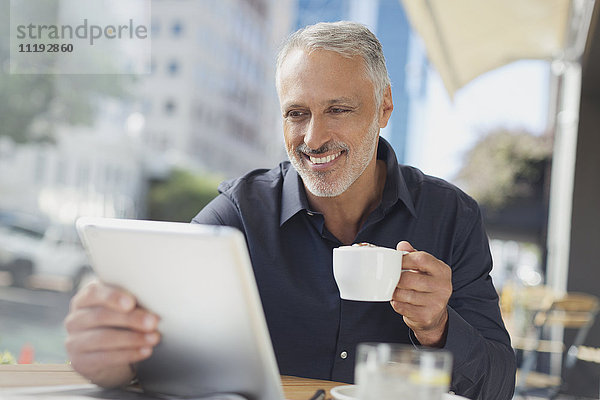 Lächelnder Geschäftsmann mit digitalem Tablet  der in einem Straßencafé Kaffee trinkt
