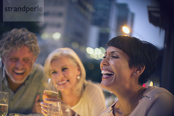 Lachende Freunde trinken Weißwein in einem urbanen Straßencafé