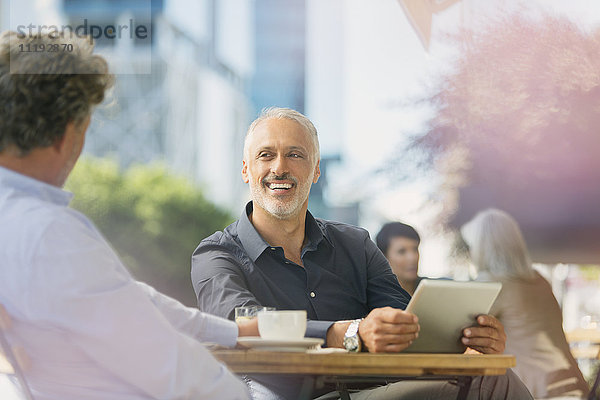 Lächelnde Geschäftsleute  die sich unterhalten  Kaffee trinken und ein digitales Tablet in einem Straßencafé benutzen