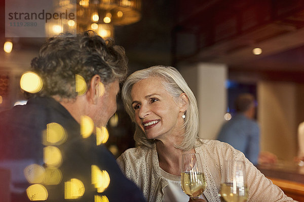 Zärtlich lächelndes älteres Paar trinkt Weißwein in einer Bar