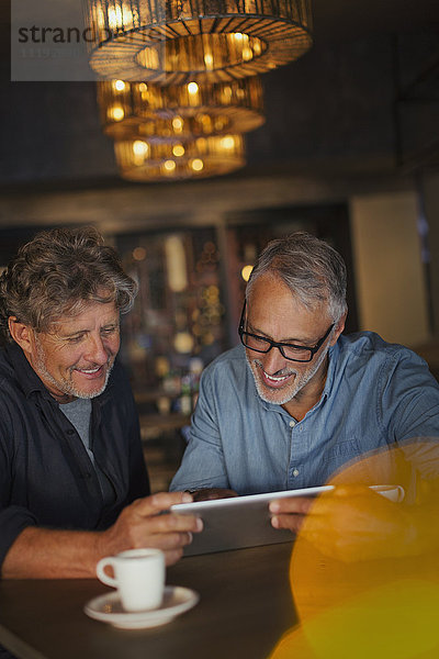 Männer  die ein digitales Tablet benutzen und am Restauranttisch Kaffee trinken