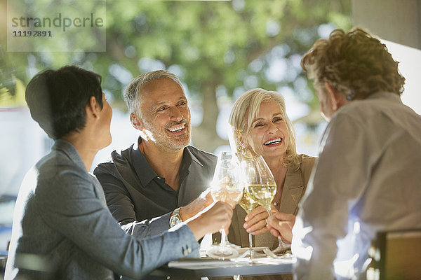 Paare stoßen mit Weißweingläsern am sonnigen Restauranttisch an