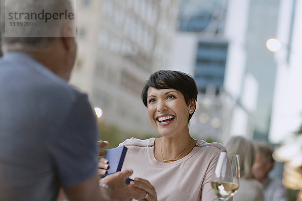 Lächelnde Frau  die ein Geschenk von ihrem Mann in einem Straßencafé erhält