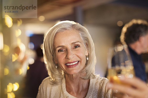 Porträt lächelnde ältere Frau stößt mit einem Weißweinglas an der Bar an