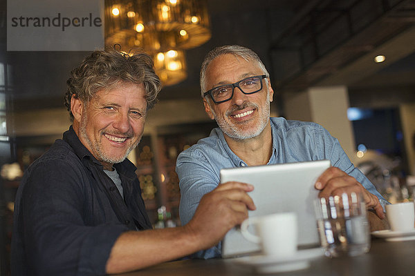 Porträt eines lächelnden Mannes  der ein digitales Tablet benutzt und am Restauranttisch Kaffee trinkt