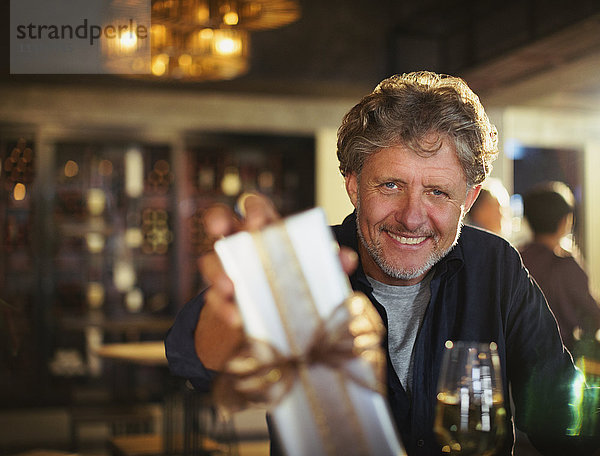 Porträt lächelnder älterer Mann  der in einer Bar ein Geschenk überreicht