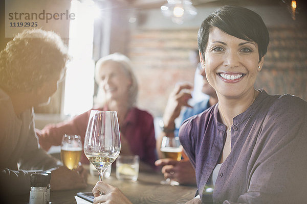 Porträt einer lächelnden Frau  die Weißwein trinkt und mit Freunden an einem Restauranttisch speist
