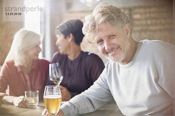 Porträt eines lächelnden älteren Mannes  der mit Freunden an einem Restauranttisch Bier trinkt
