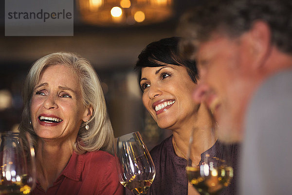 Lächelnde Frauen trinken Weißwein an einer Bar