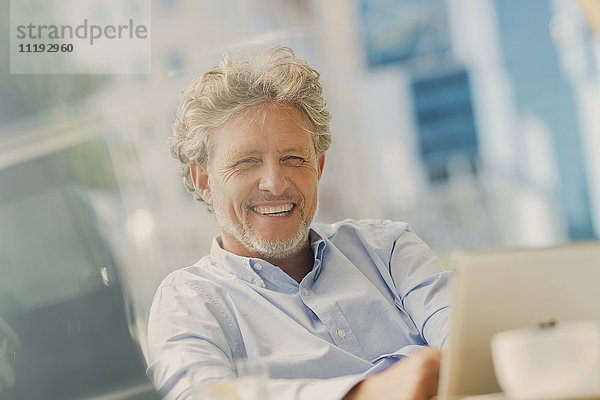 Porträt eines lächelnden Geschäftsmanns  der ein digitales Tablet in einem Straßencafé benutzt
