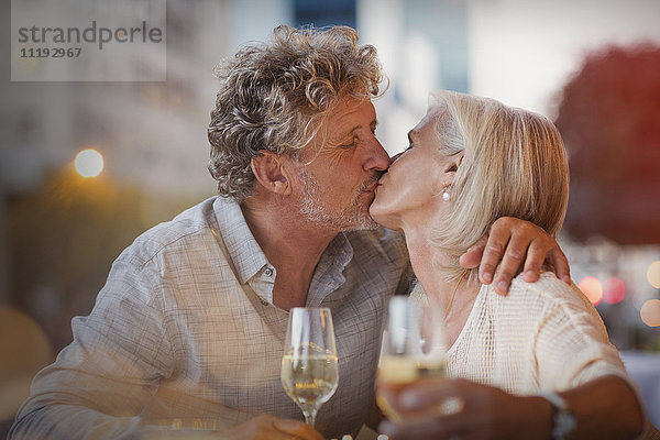 Zärtliches älteres Paar  das sich küsst und Weißwein in einem Straßencafé trinkt