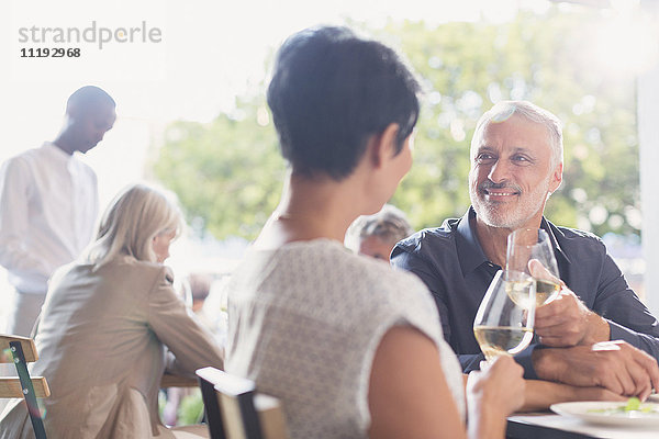 Ein Paar unterhält sich und trinkt Weißwein am Tisch eines Restaurants im Freien
