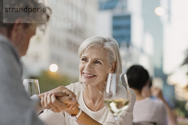 Zärtliches älteres Paar hält sich an den Händen und trinkt Weißwein in einem städtischen Straßencafé