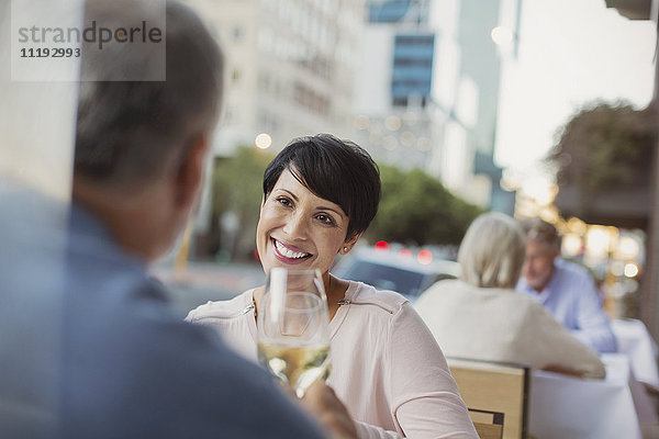 Lächelndes Paar stößt mit Weißweingläsern in einem Straßencafé an