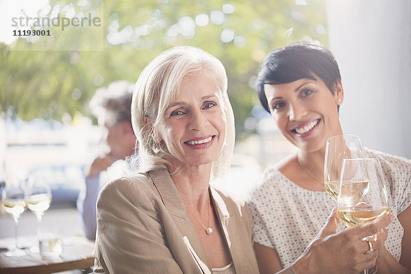 Portrait lächelnde Mutter und Tochter stoßen mit Weißweingläsern in einem sonnigen Restaurant an