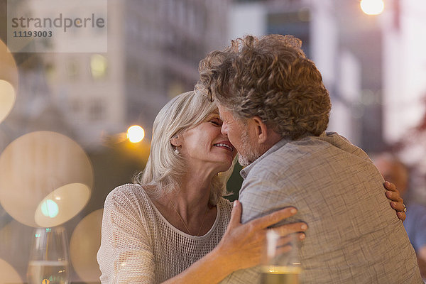 Zärtliches älteres Paar küsst sich in einem städtischen Straßencafé
