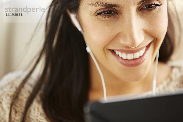 Nahaufnahme einer lächelnden Frau  die ein digitales Tablet mit Kopfhörern benutzt
