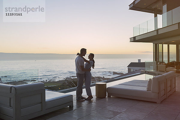 Zärtliches Paar  das sich auf einer luxuriösen Terrasse mit Meerblick umarmt