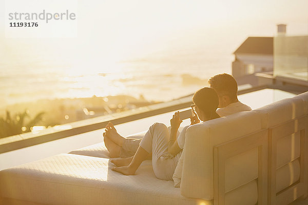 Silhouette Paar mit Handy auf Chaiselongue mit Sonnenuntergang Meerblick