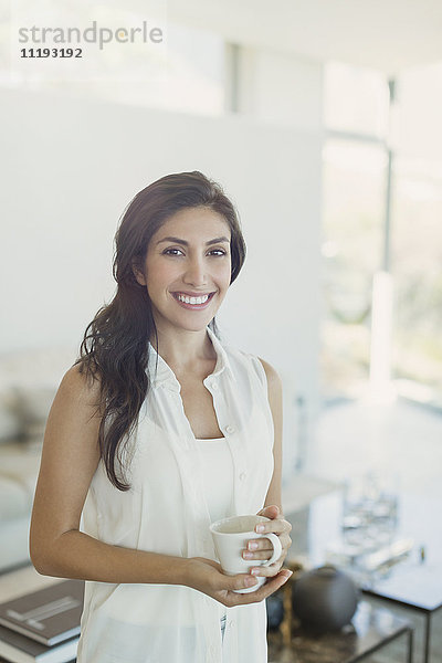 Portrait lächelnde brünette Frau trinkt Kaffee im Wohnzimmer