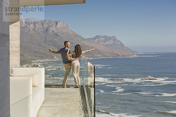 Unbekümmertes Paar auf sonnigem Luxusbalkon mit Blick auf Meer und Berge