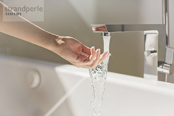 Frau berührt Wasser aus modernem Badewannenwasserhahn