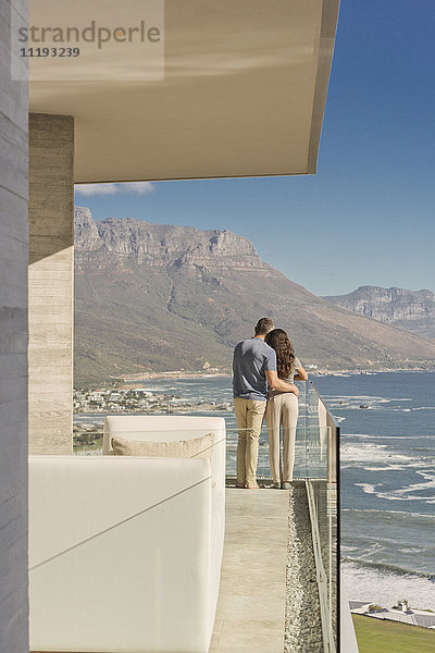 Paar mit Blick auf das sonnige Meer und die Berge vom luxuriösen Balkon