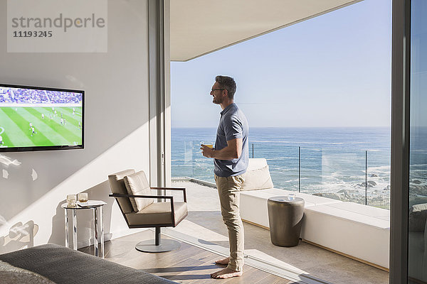 Mann schaut Fußball im Fernsehen an sonniger Luxus-Terrassentür mit Meerblick