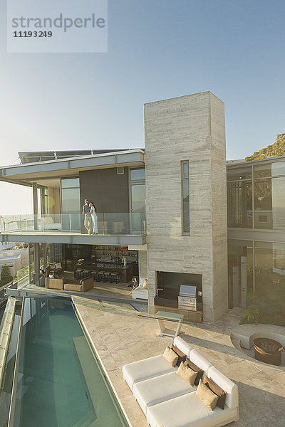 Paar steht auf einem sonnigen  modernen  luxuriösen Balkon über dem Pool.