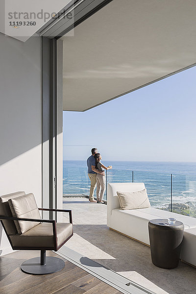 Ein Paar genießt den sonnigen Blick auf das Meer vom Balkon eines luxuriösen Hauses